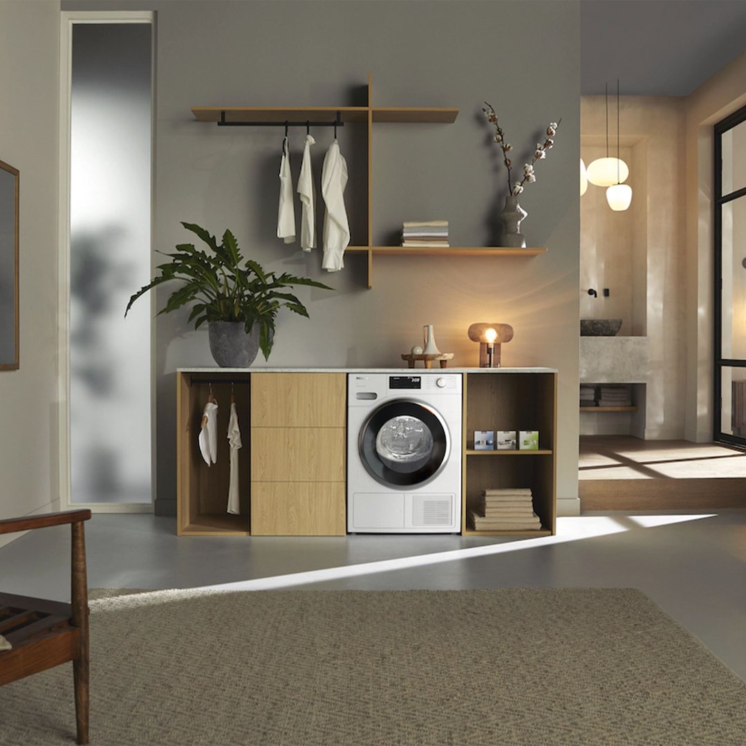 Heat pump dryer integrated into a wooden laundry cabinet in a modern room