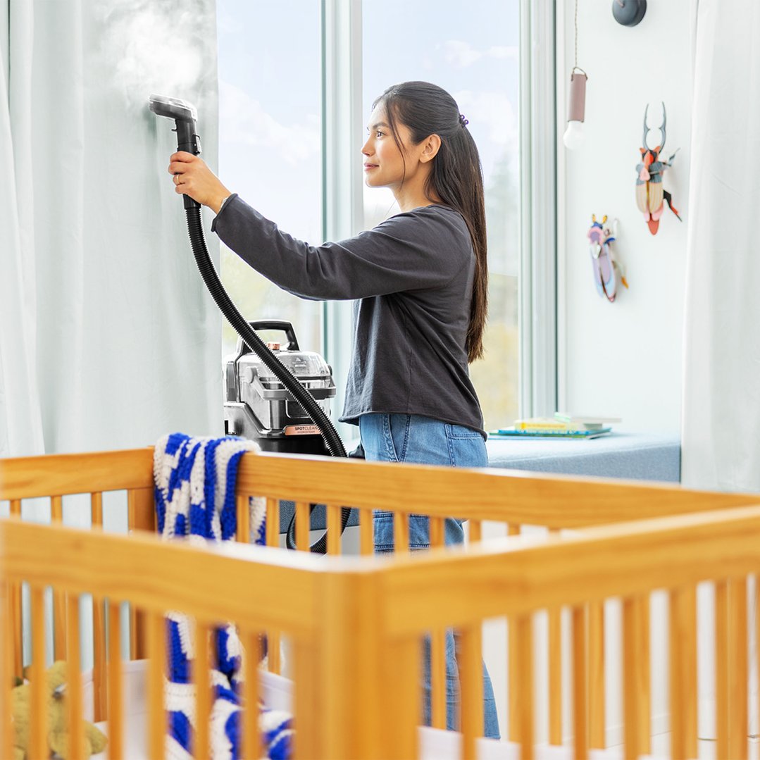 Woman using a BISSELL SpotClean HydroSteam vacuum cleaner to steam clean curtains
