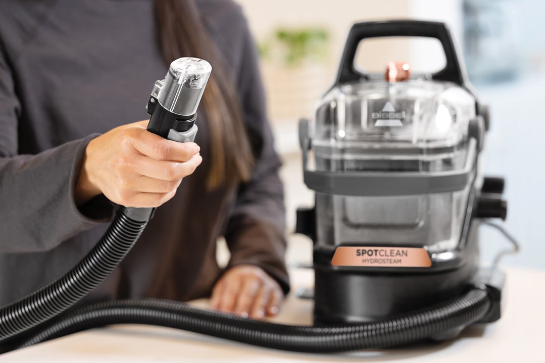 Woman holding the hose attachment of a BISSELL SpotClean HydroSteam vacuum cleaner