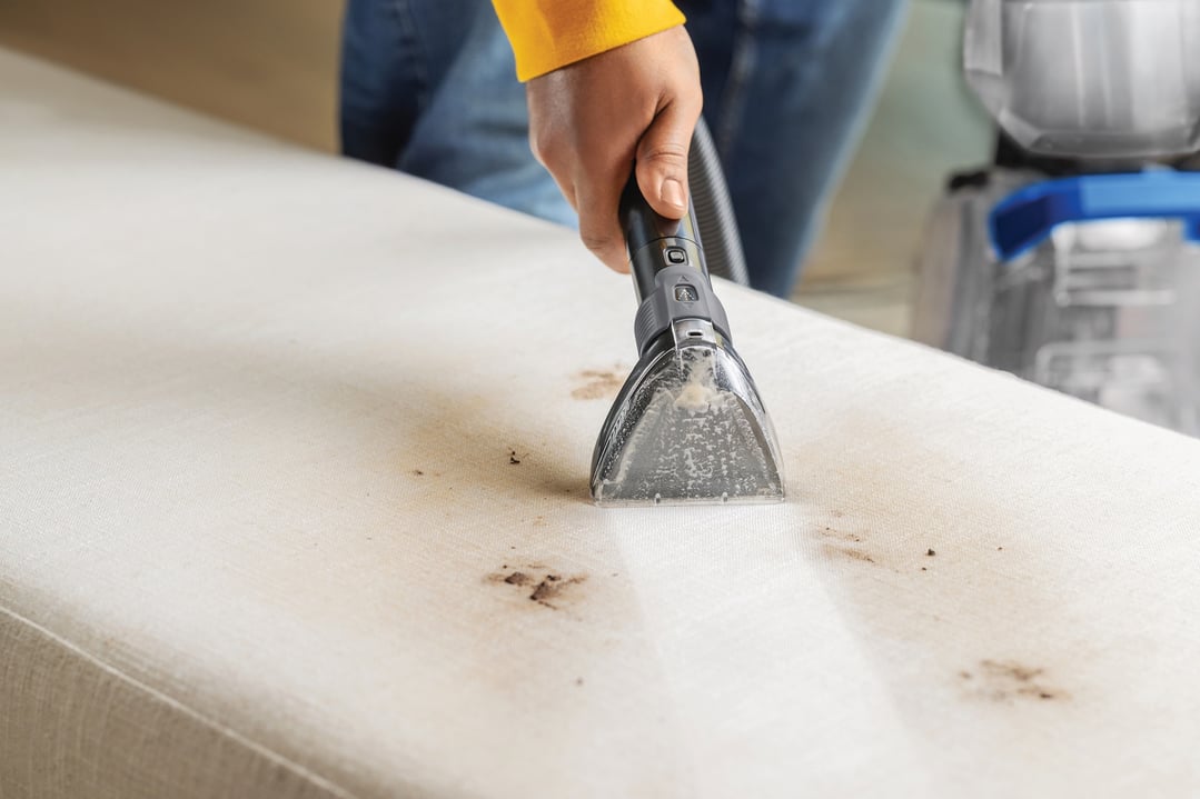 Hand using a BISSELL vacuum cleaner to clean stains from a white mattress