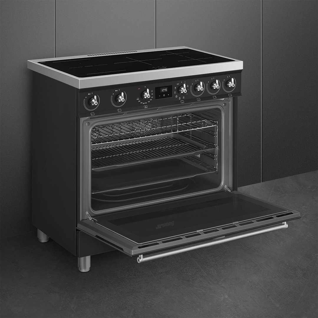 Matte black freestanding cooker with oven door open in a dark kitchen