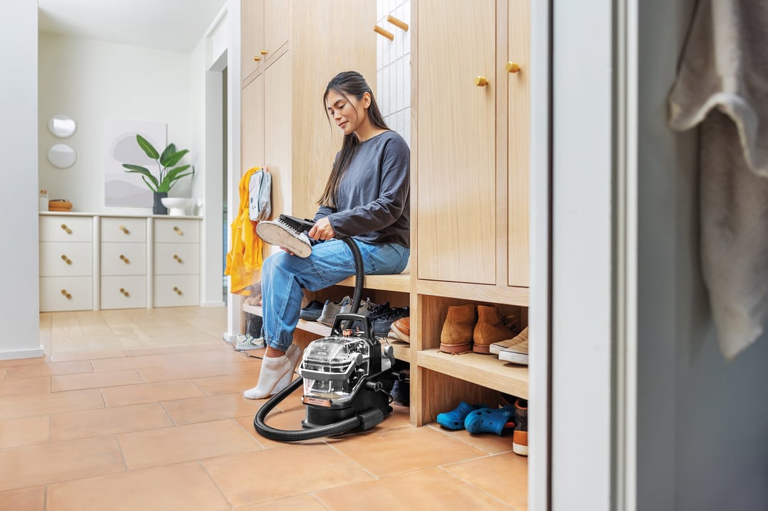 Woman cleaning a shoe with a BISSELL SpotClean HydroSteam vacuum cleaner