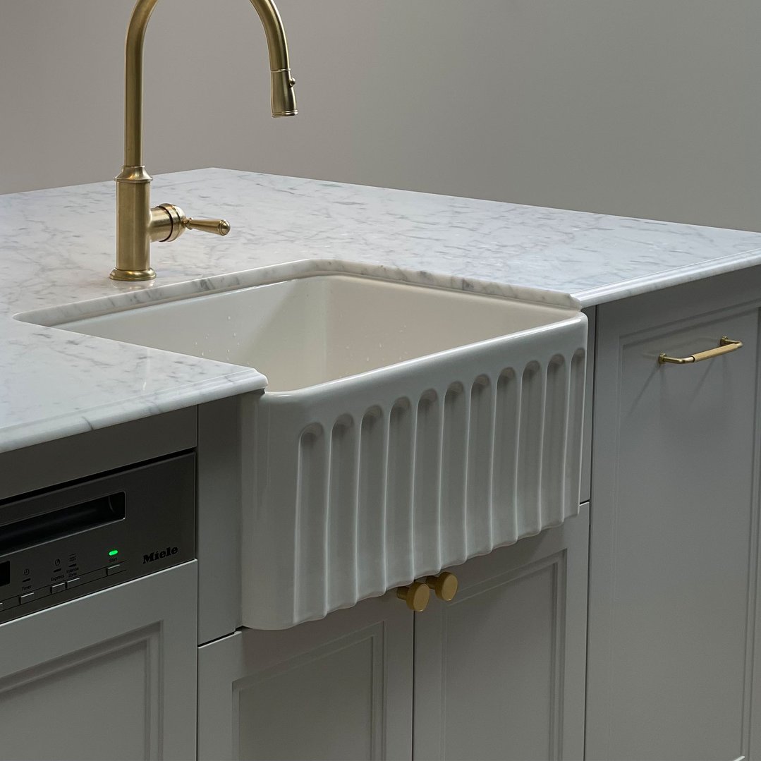 White fireclay butler sink with gold faucet and dishwasher in a modern kitchen