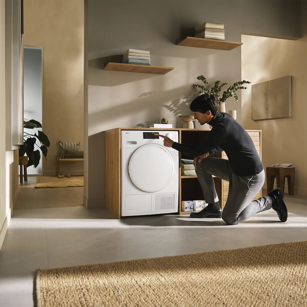 Man kneeling to operate the heat pump dryer in a modern laundry room