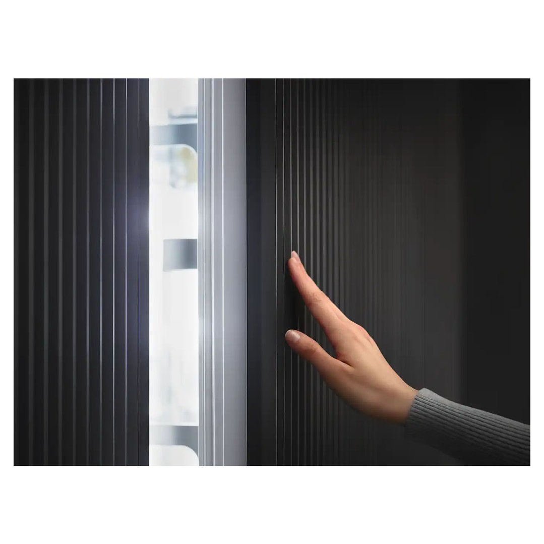 Hand touching the dark panel of a freezer with an illuminated interior