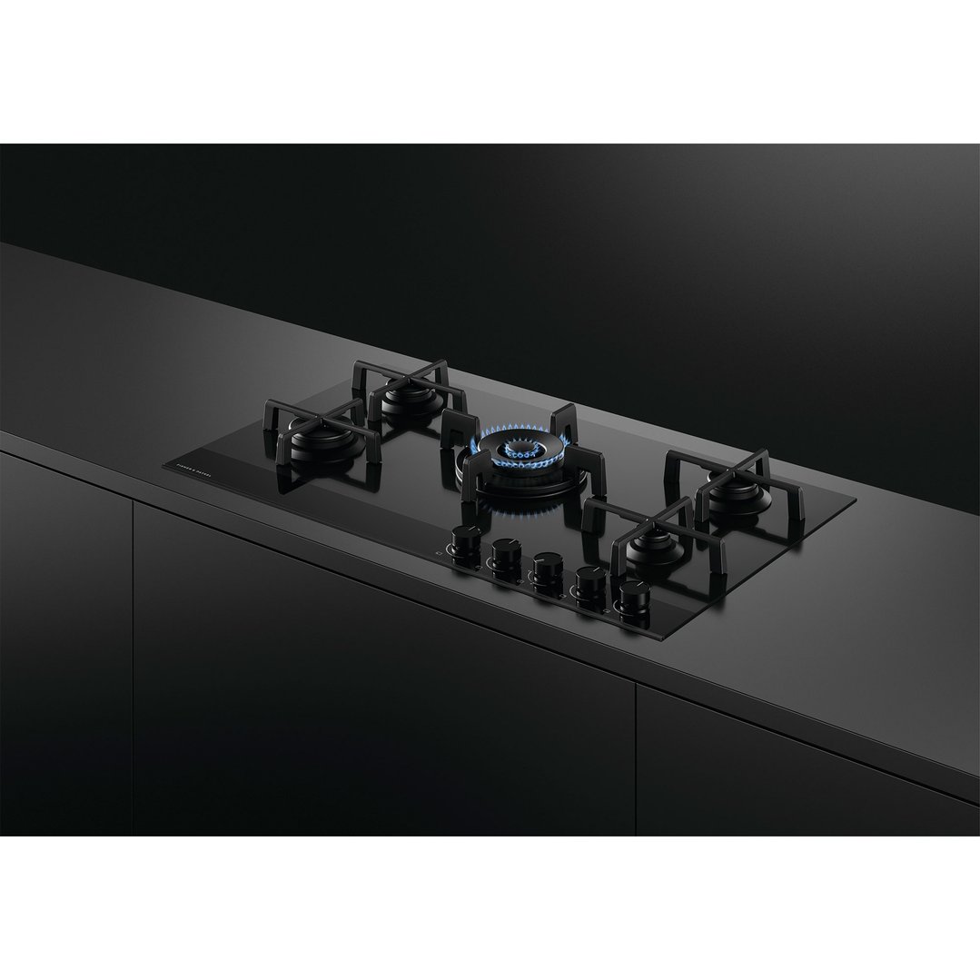 Black gas on glass cooktop with five burners and controls in a dark kitchen