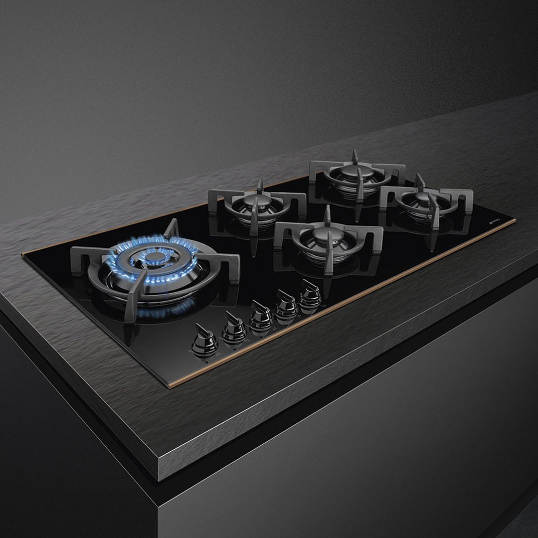 Black gas cooktop with five burners, one with blue flame, on a dark countertop
