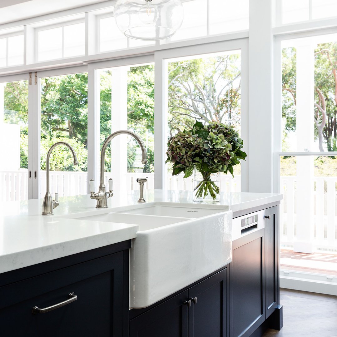 White fireclay butler sink with two faucets in a modern kitchen setting