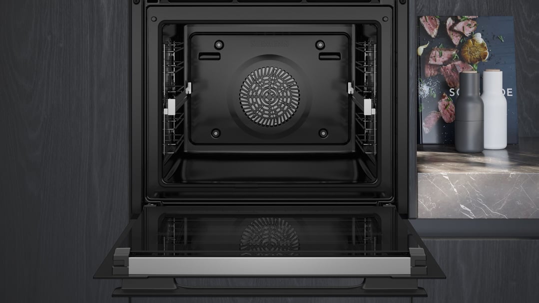 Open black Siemens oven with a cookbook and two shakers on a marble benchtop