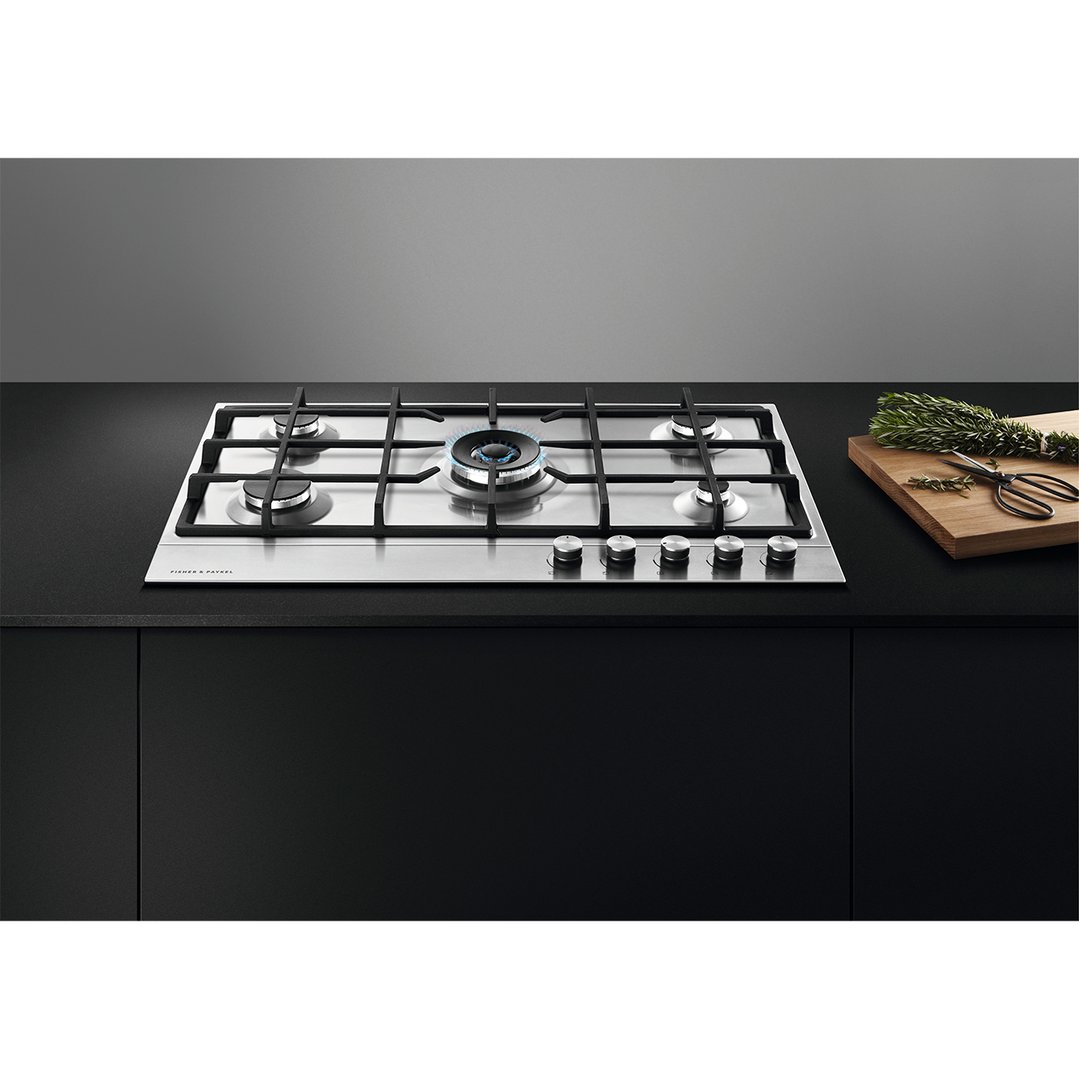 Stainless steel gas cooktop with one burner lit, on a black countertop