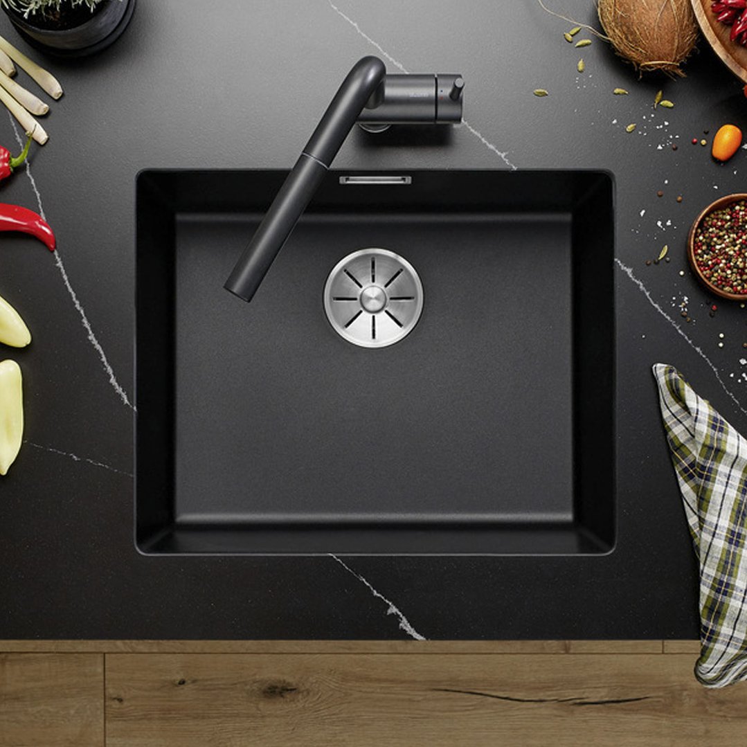 Black single bowl undermount sink with tap in a kitchen setting with spices