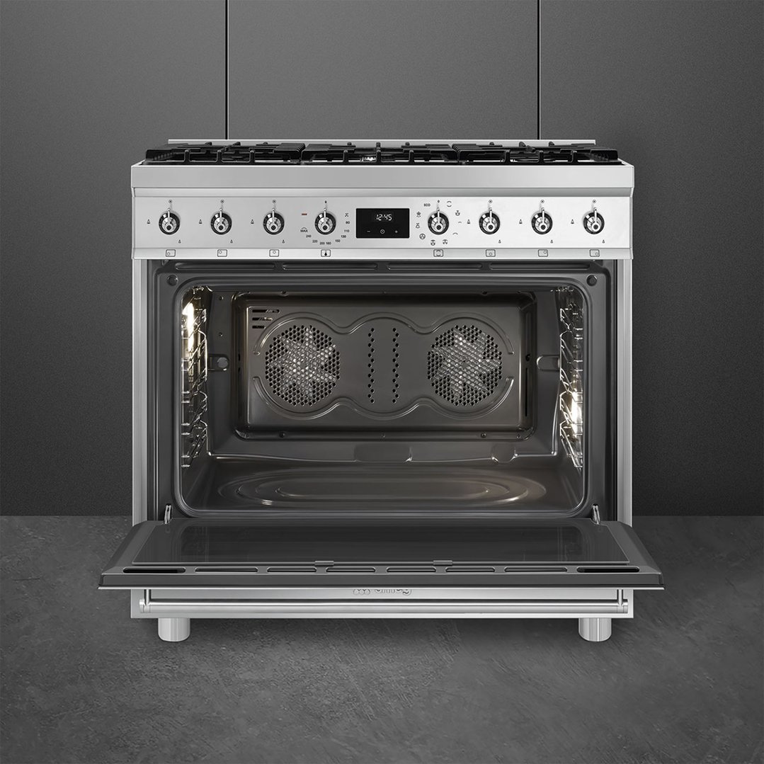 Stainless steel freestanding cooker with oven door open in a dark kitchen setting