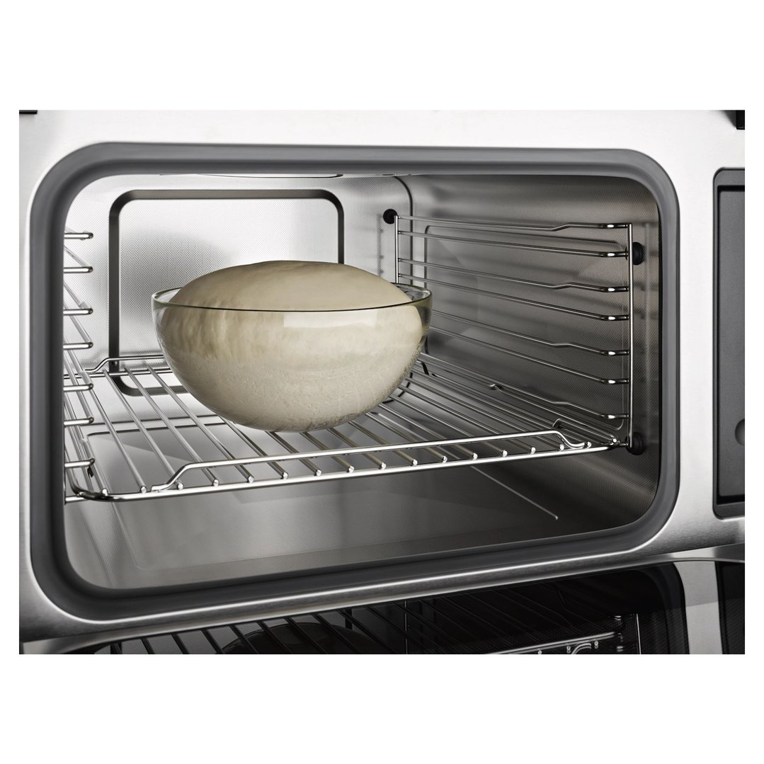 Glass bowl of dough rising on a rack inside a microwave oven
