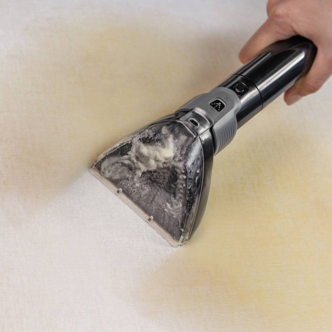 Hand using a carpet and upholstery cleaner on a light-colored surface