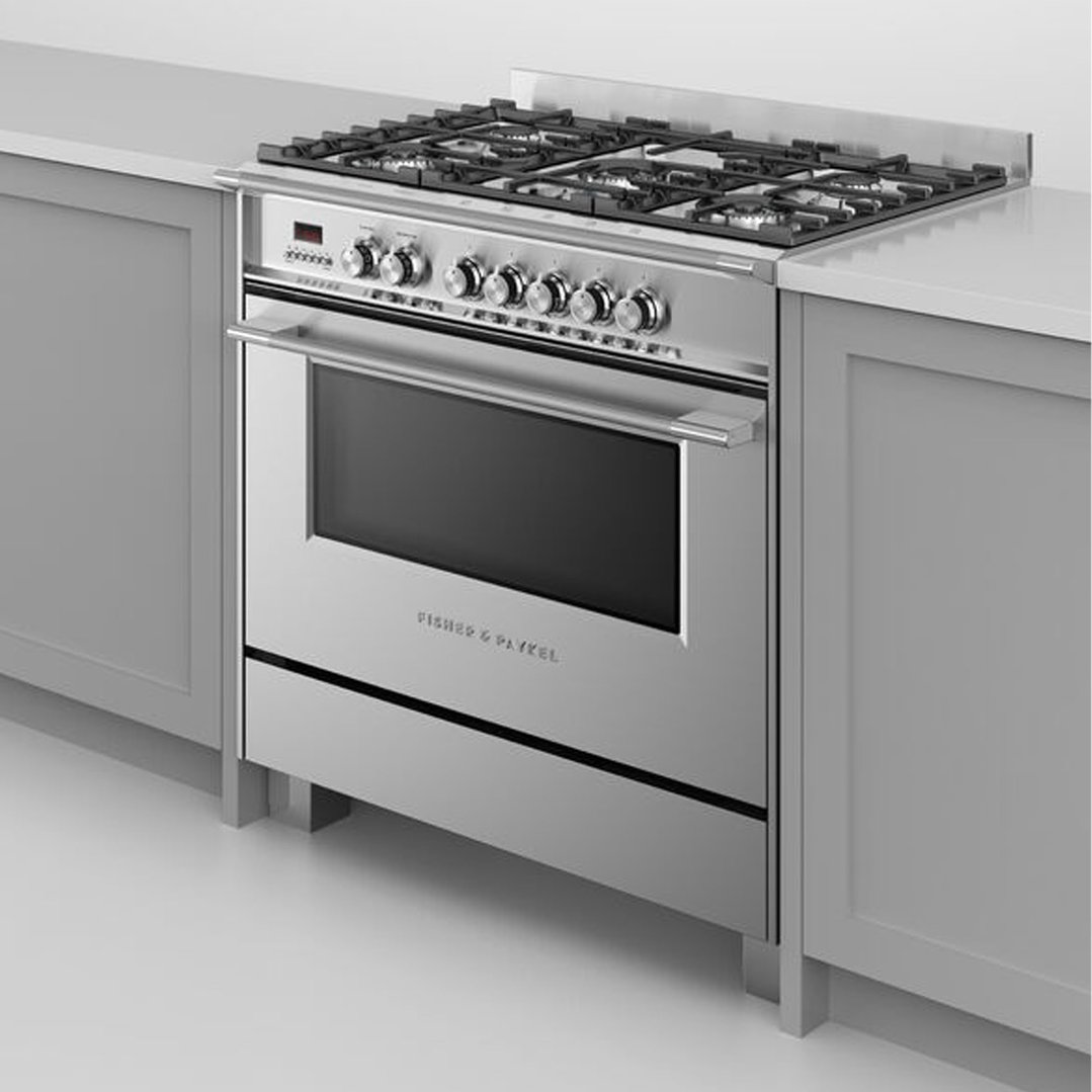 Stainless steel dual fuel cooker with five burners and an oven in a kitchen setting