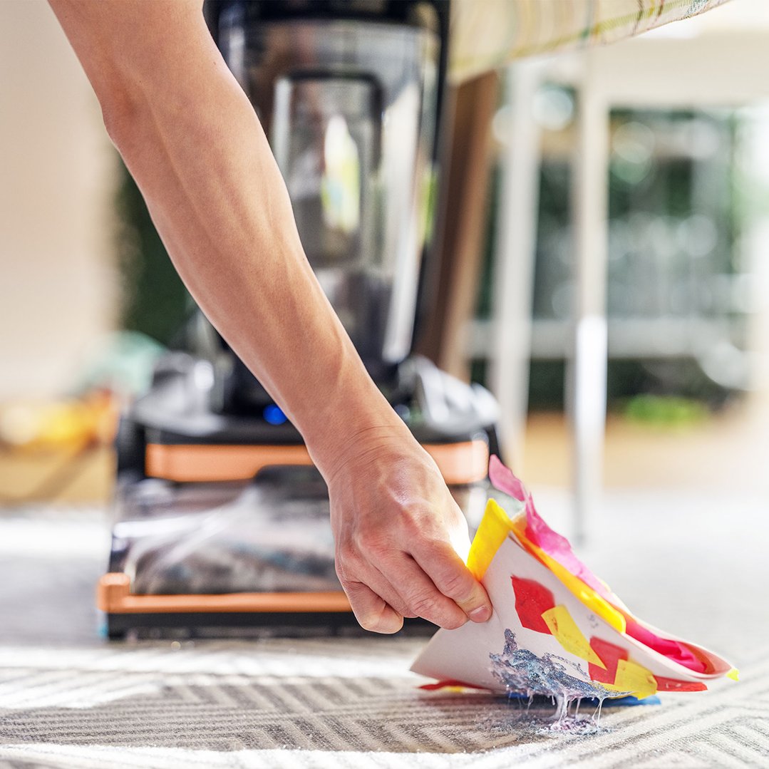 Person cleaning up glitter and paper scraps from a carpet with a vacuum cleaner