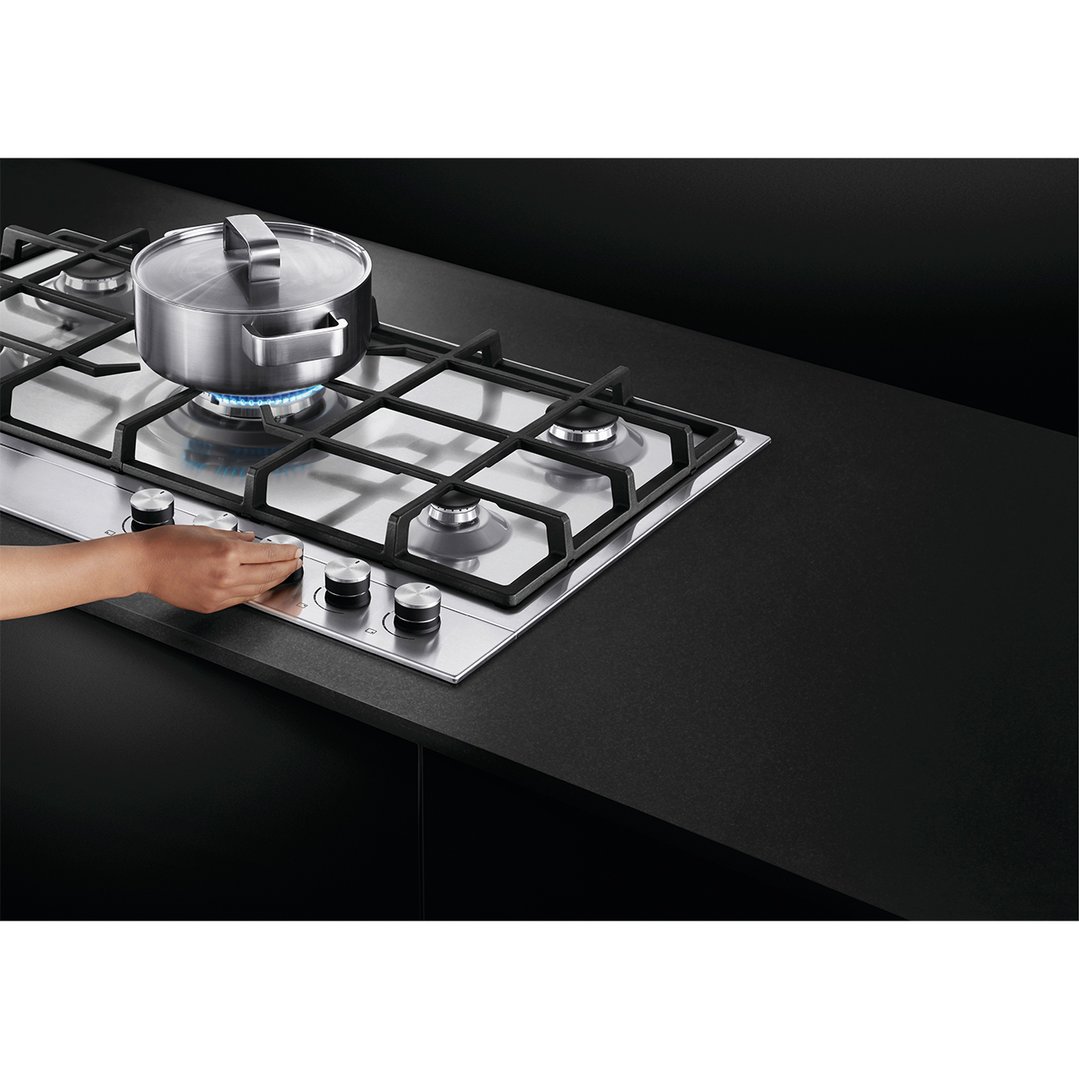 Hand adjusting controls on a stainless steel gas cooktop with a pot