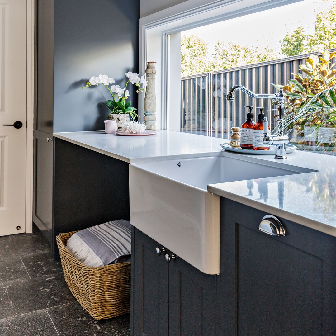 White fireclay butler sink in a dark grey laundry with a window view