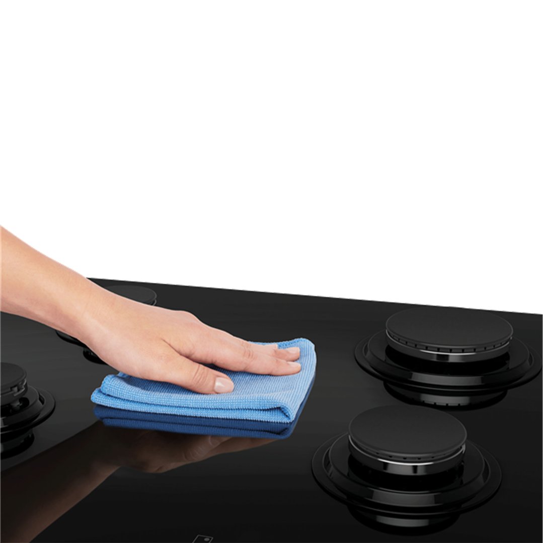 Hand cleaning a black ceramic glass gas cooktop with a blue cloth