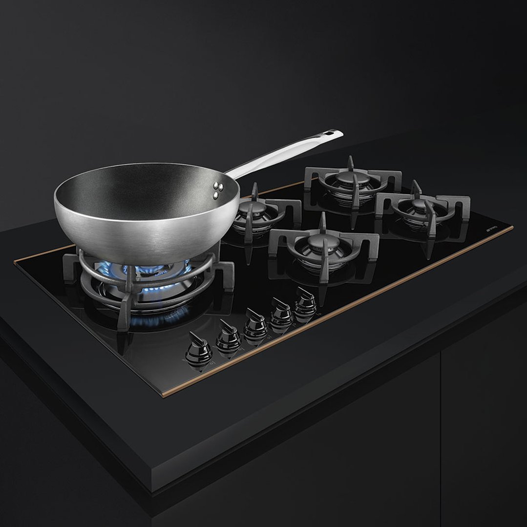A wok on a gas cooktop with five burners in a dark kitchen