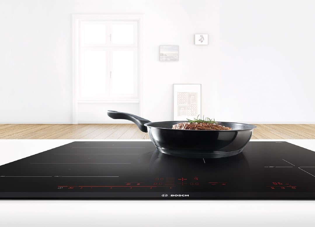 Black Bosch induction cooktop with a pan of food in a modern kitchen