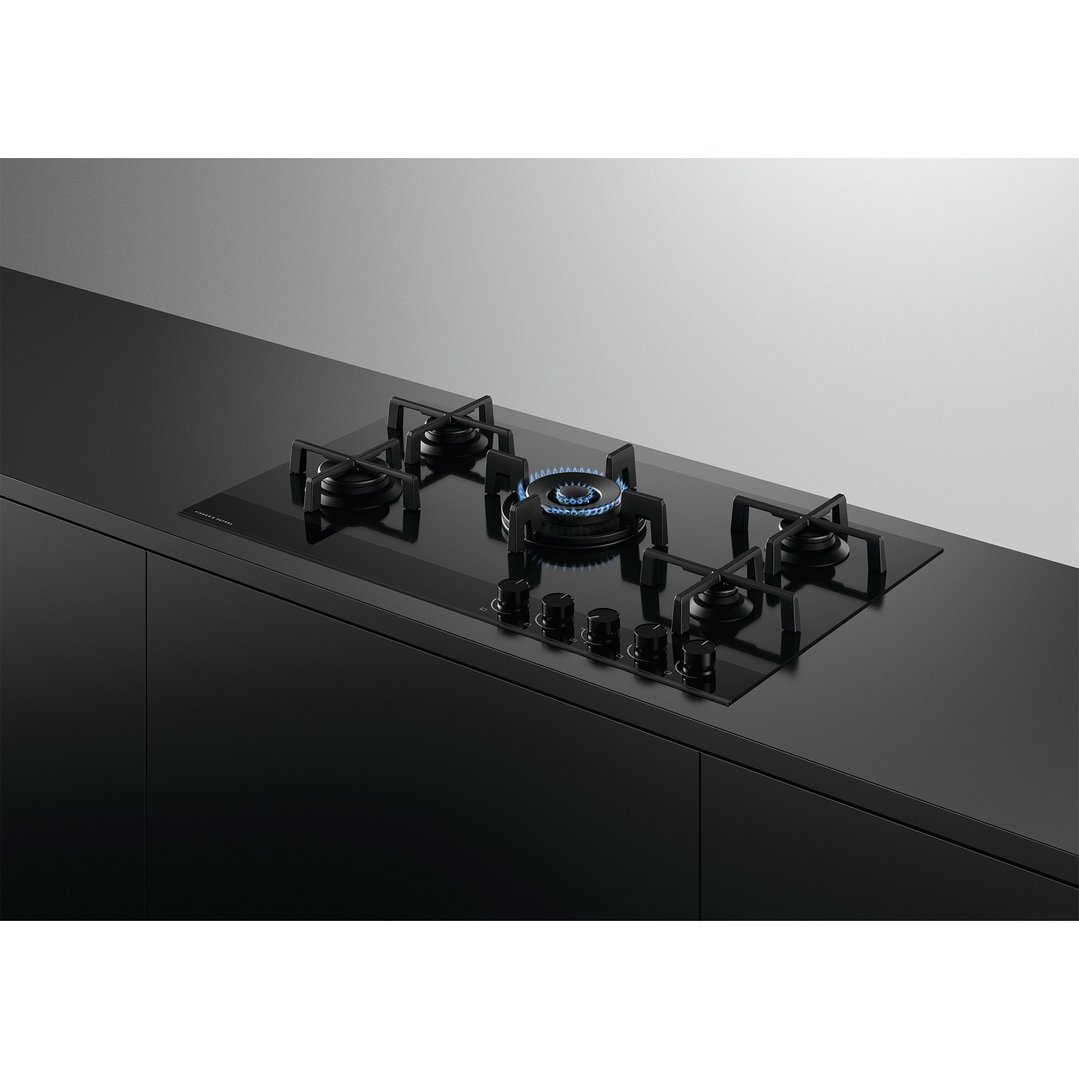 Black gas on glass cooktop with five burners, one lit, in a modern kitchen