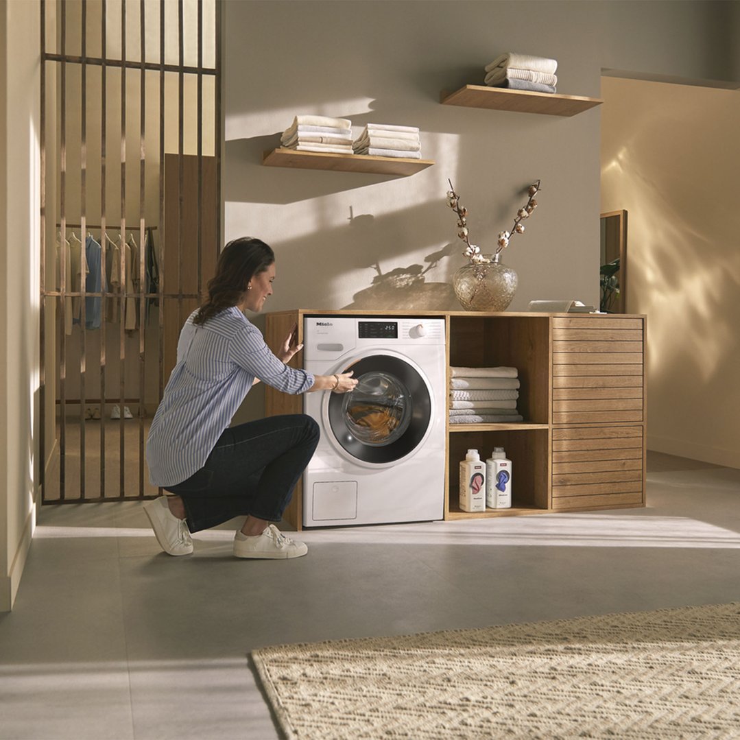 Woman loading laundry into a white front load washing machine in a laundry room