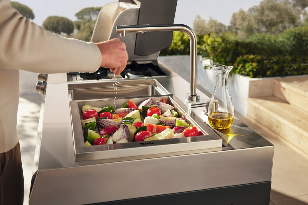 Person seasoning vegetables in an outdoor kitchen sink module with a tap
