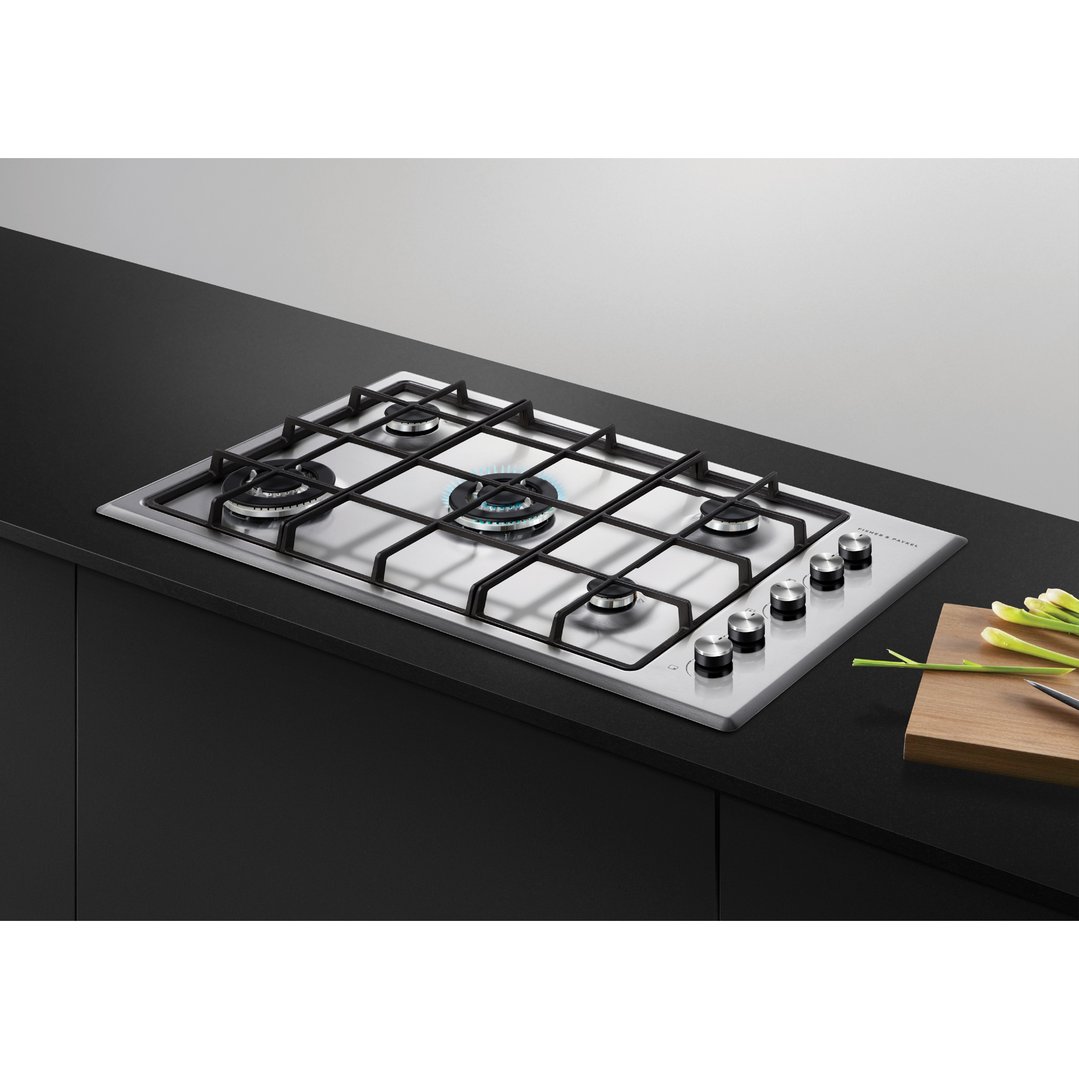Stainless steel gas cooktop with five burners, one lit, on a black countertop