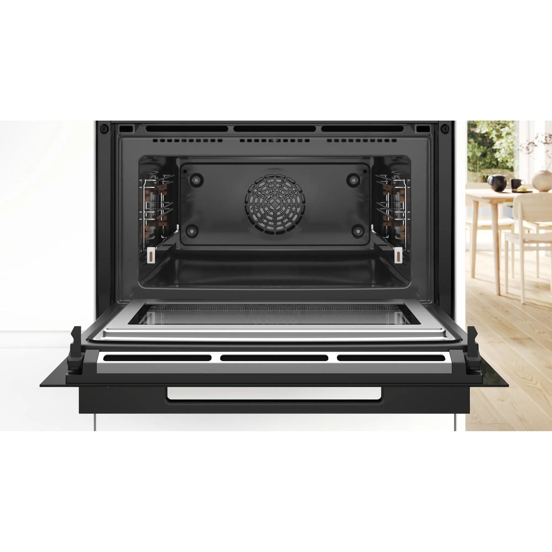 Open built-in microwave oven with a view of a dining area in the background