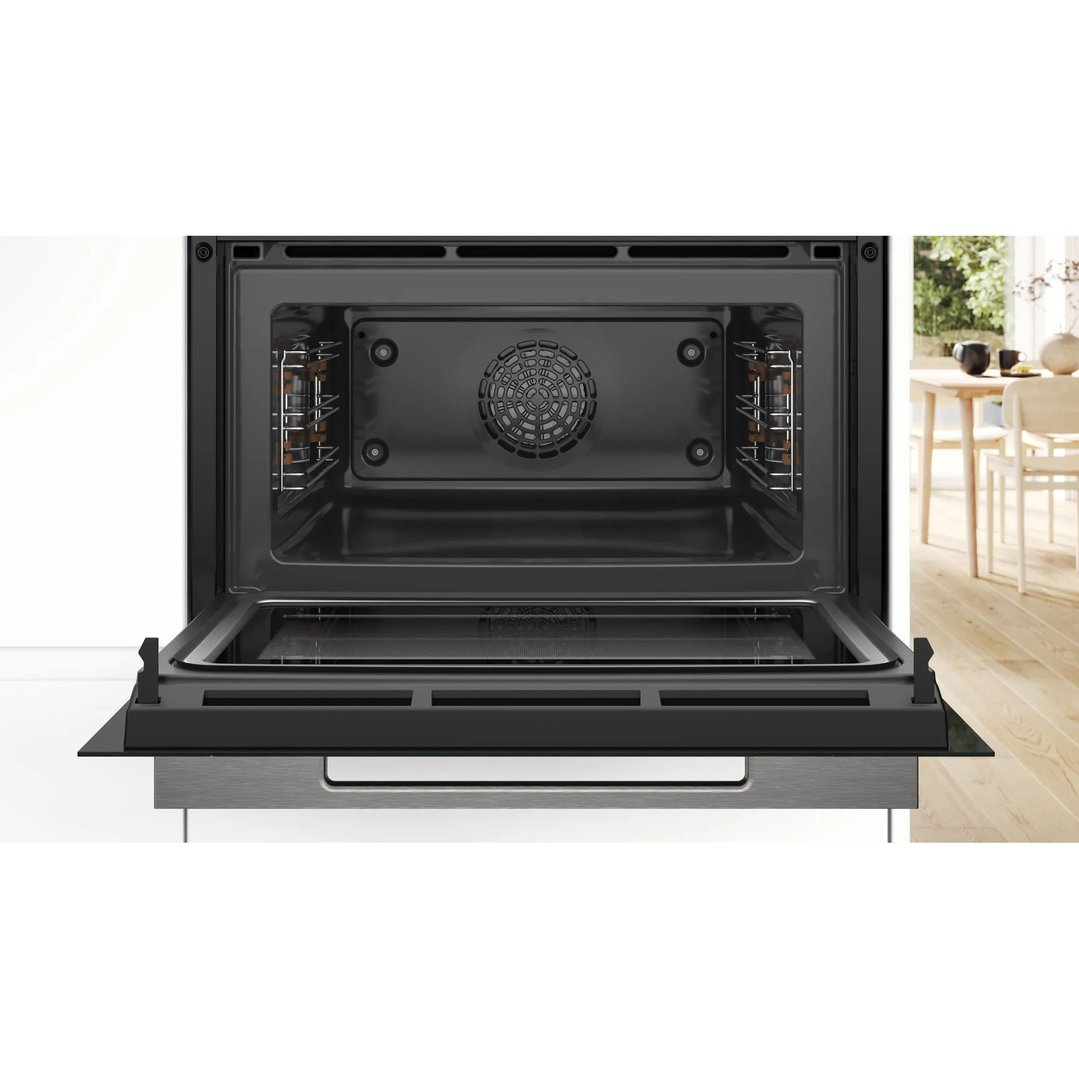 Open Bosch microwave oven with a dining area in the background