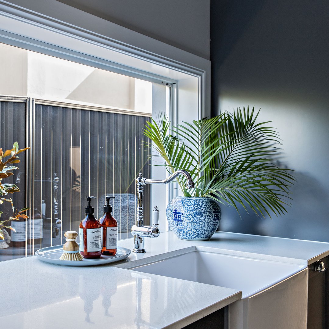 Butler sink with chrome tap, plant, and soap bottles on a white countertop