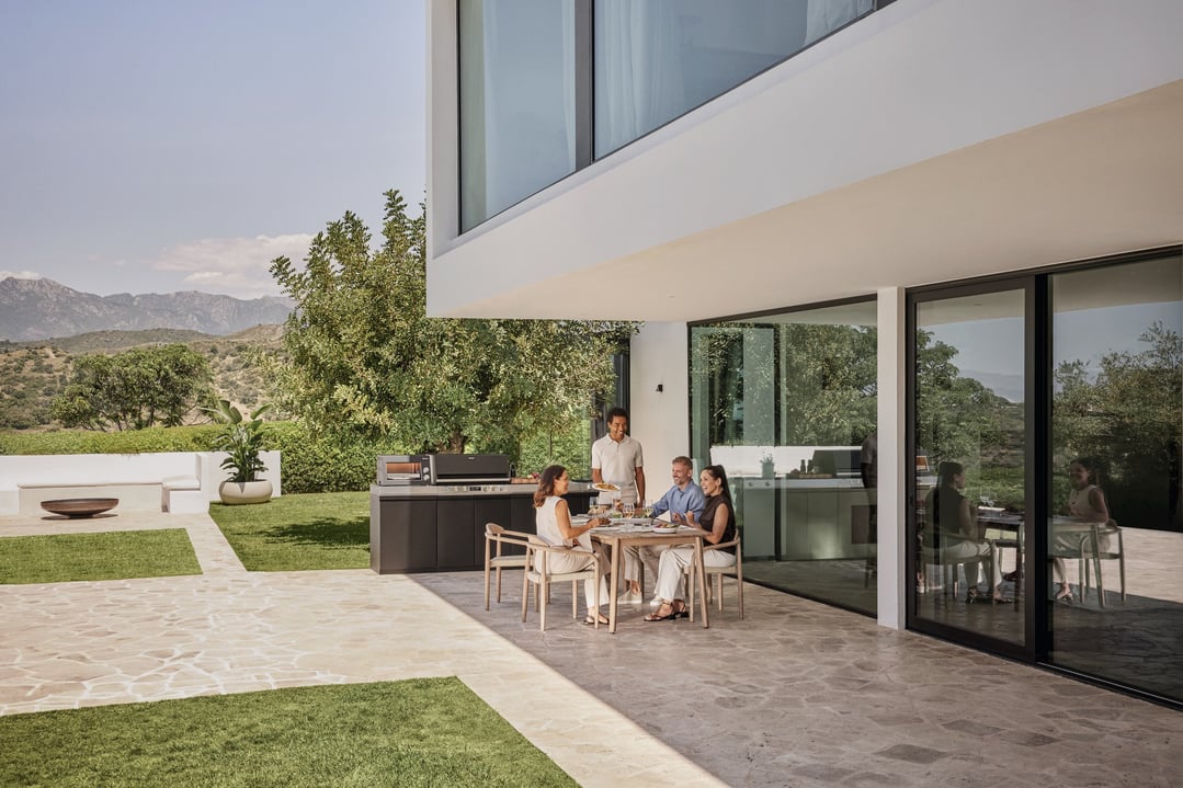 People dining outdoors with a Miele Advance Outdoor Kitchen BBQ nearby