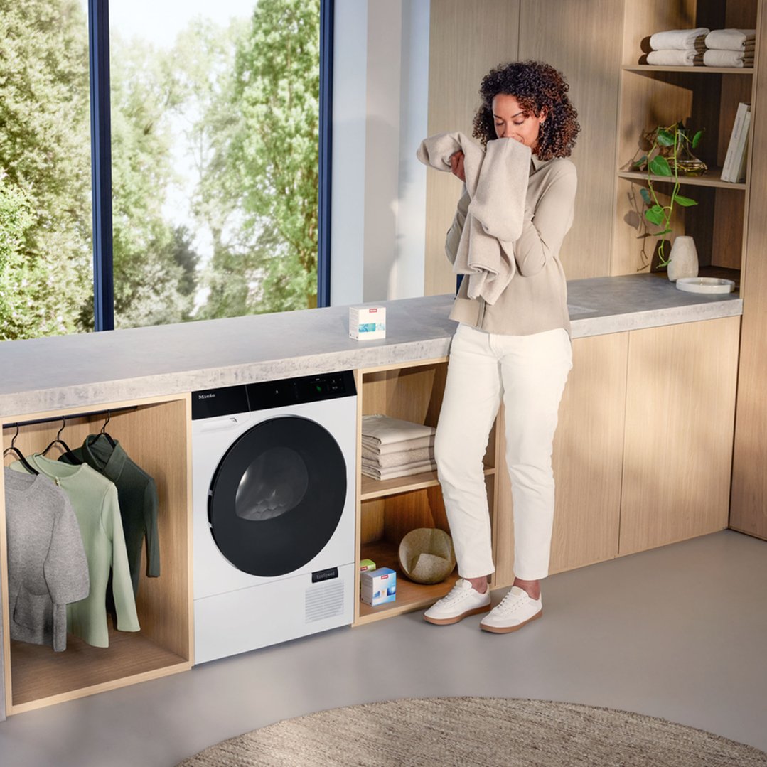 Woman smelling a freshly dried towel next to a Miele dryer in a laundry room