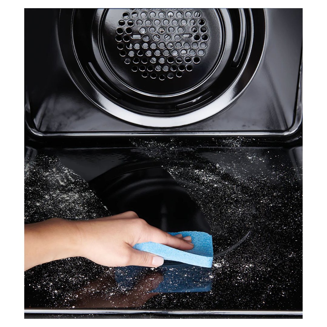 A hand cleaning the interior of a black oven with a blue sponge