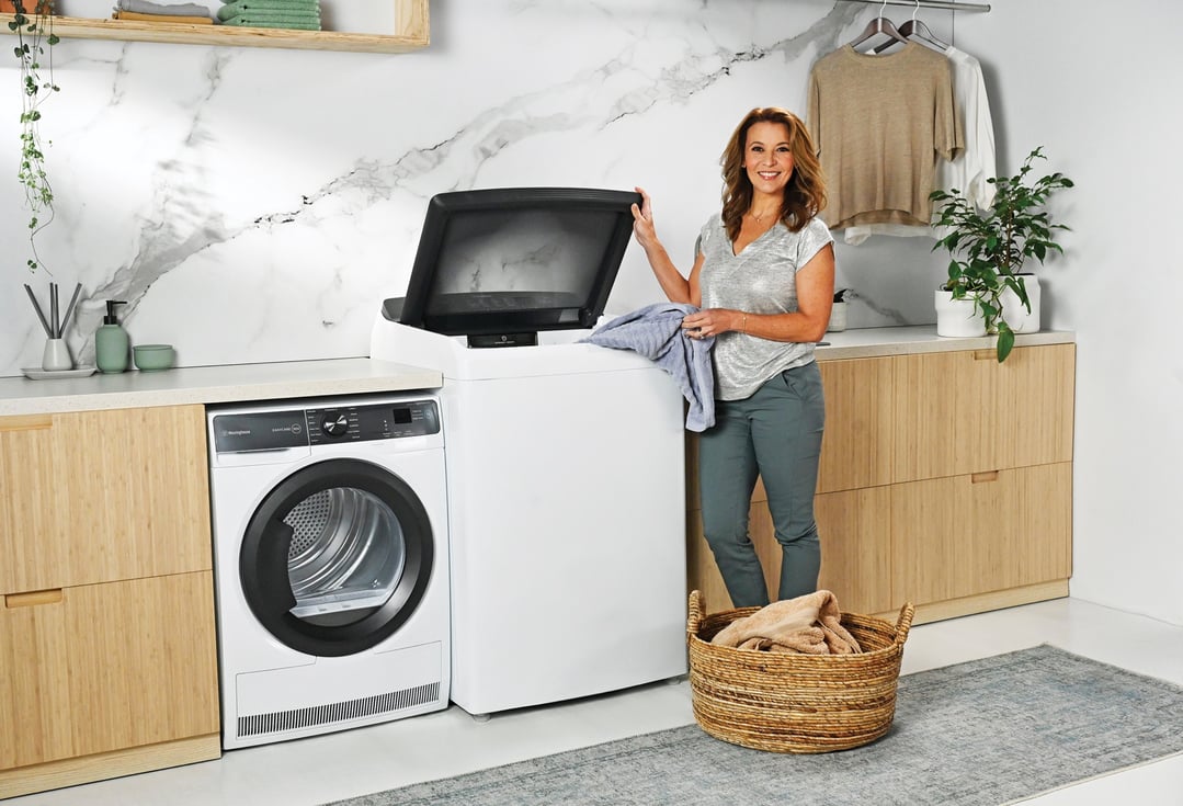 Woman loading laundry into a top load washing machine in a modern laundry room