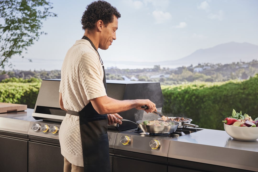 Man cooking with tongs on an outdoor barbeque cooking module with a scenic background