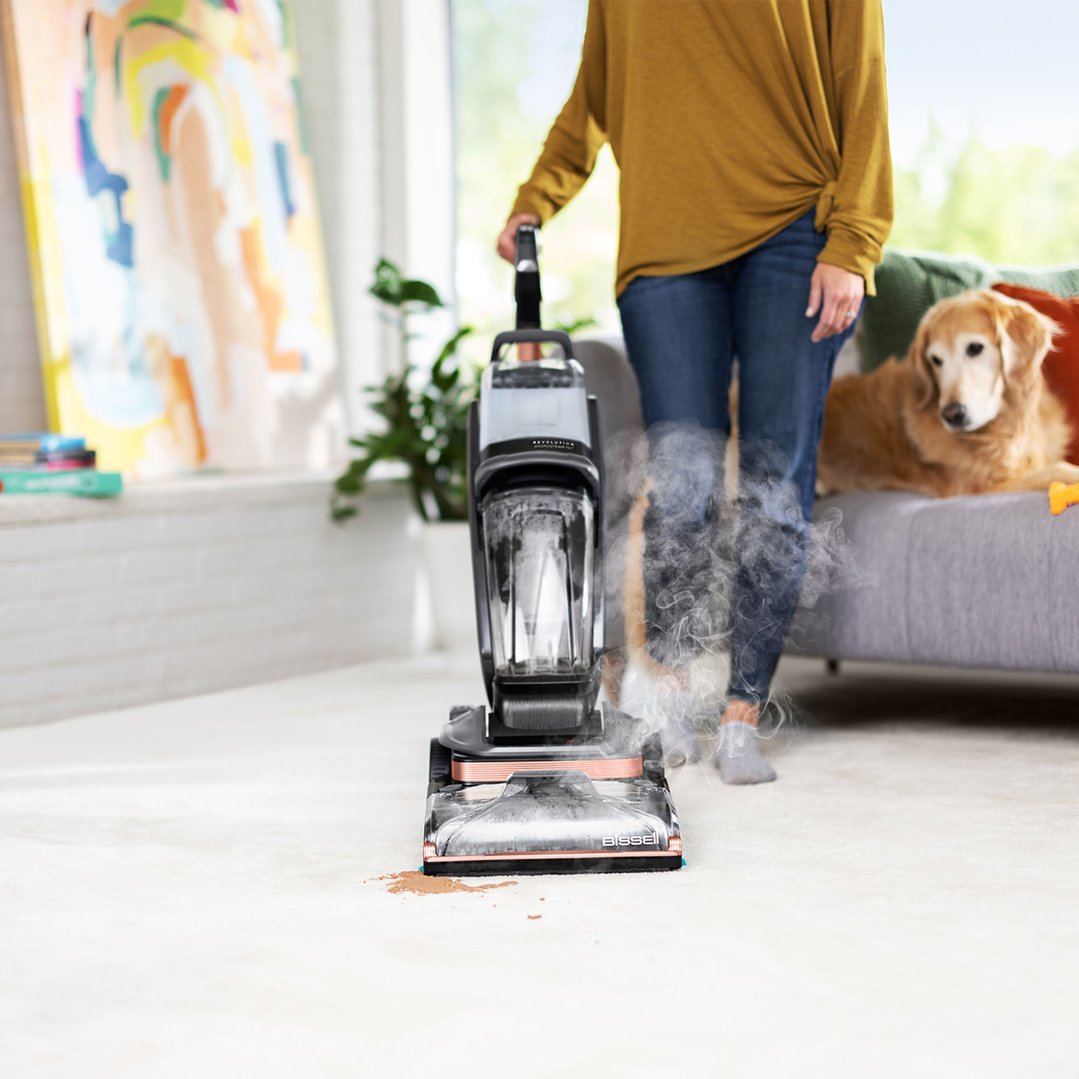 Woman using a BISSELL vacuum cleaner on a carpet with a dog nearby
