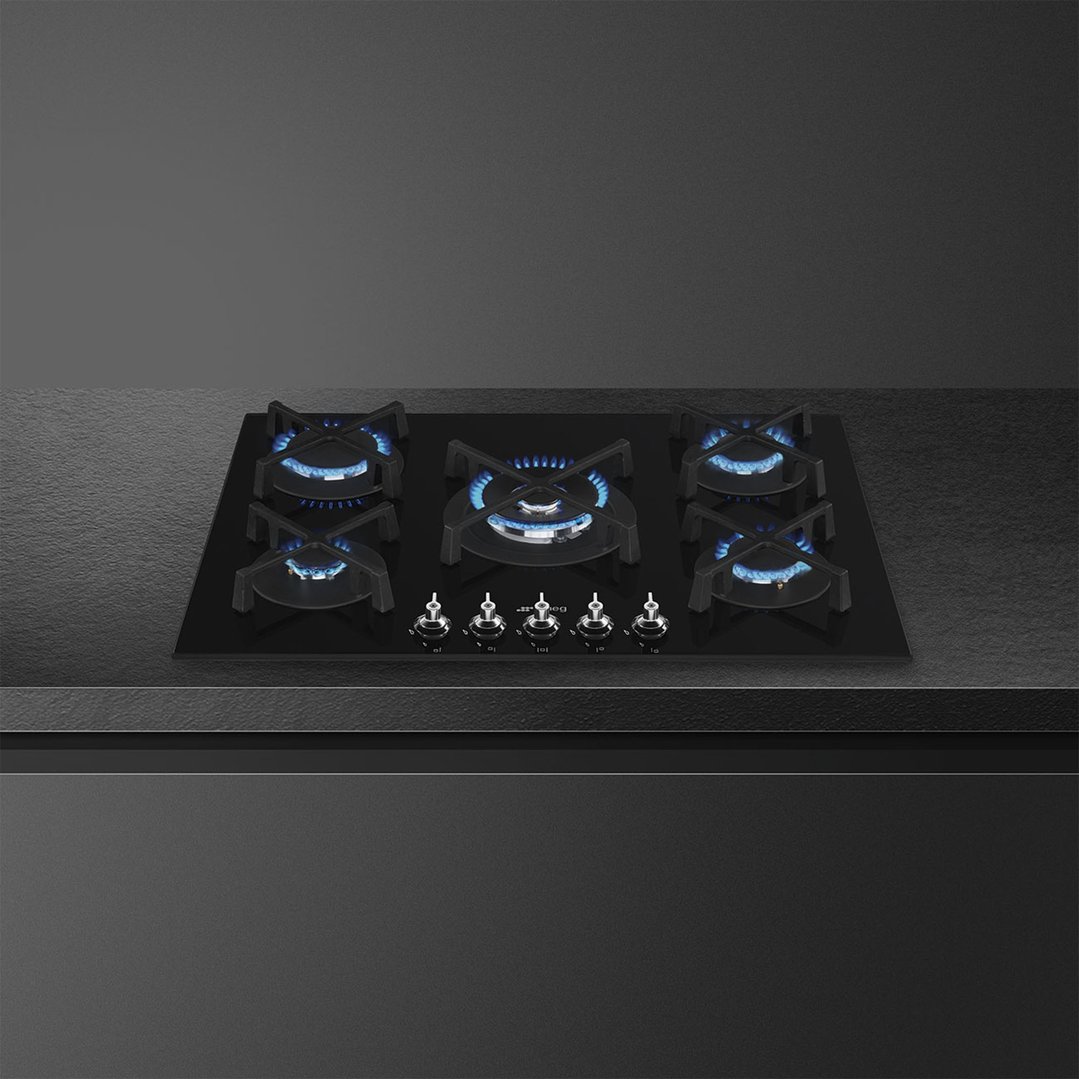 Black glass gas cooktop with five burners and controls, installed in a kitchen counter