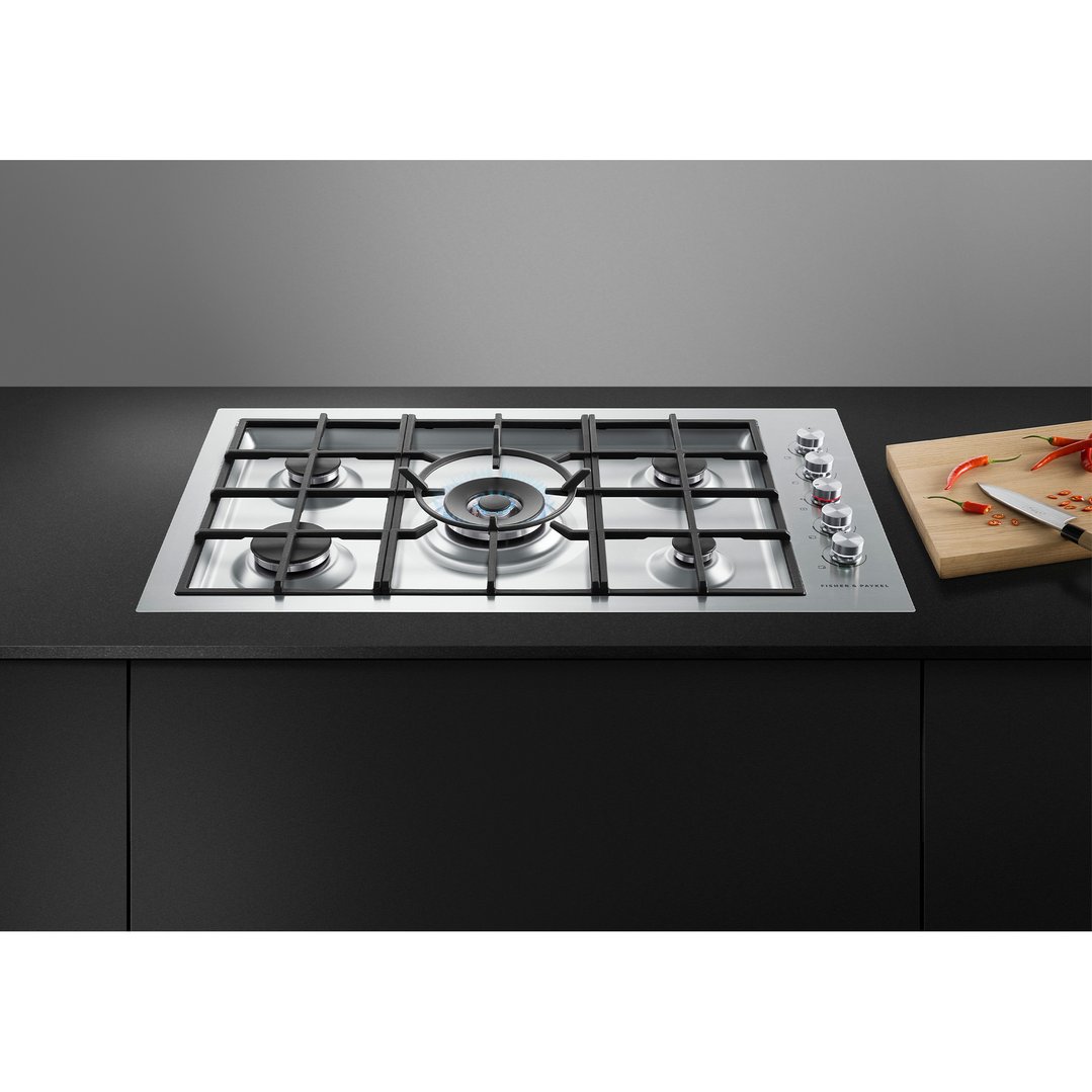 A five-burner gas cooktop with one burner lit, on a black countertop