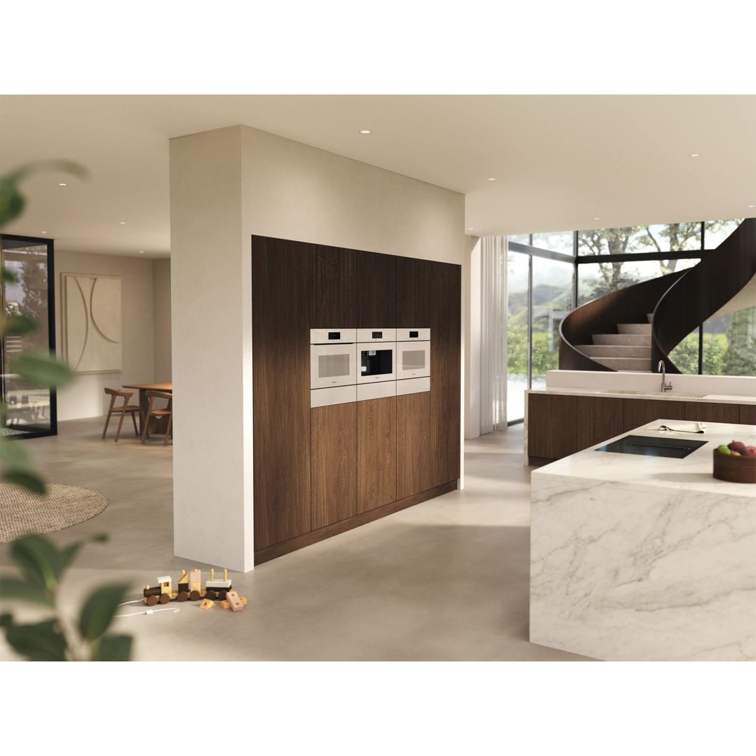 Three ovens and a coffee machine built into dark wood cabinetry in a modern kitchen