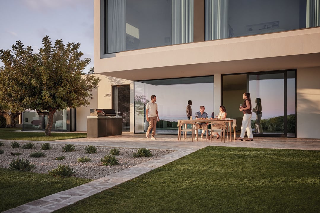 People gathered around an outdoor kitchen BBQ on a patio at sunset