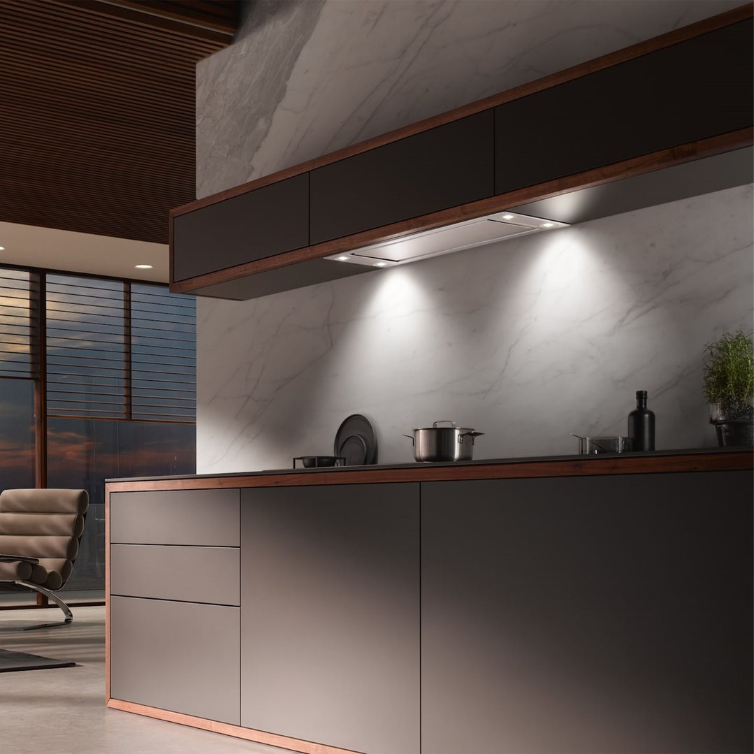 Built-in rangehood illuminating a modern kitchen with marble backsplash and dark cabinetry