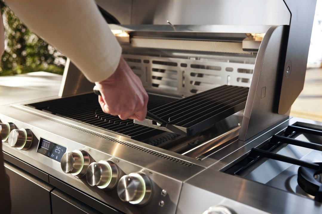 Hand placing a cast iron BBQ grate into a stainless steel outdoor grill