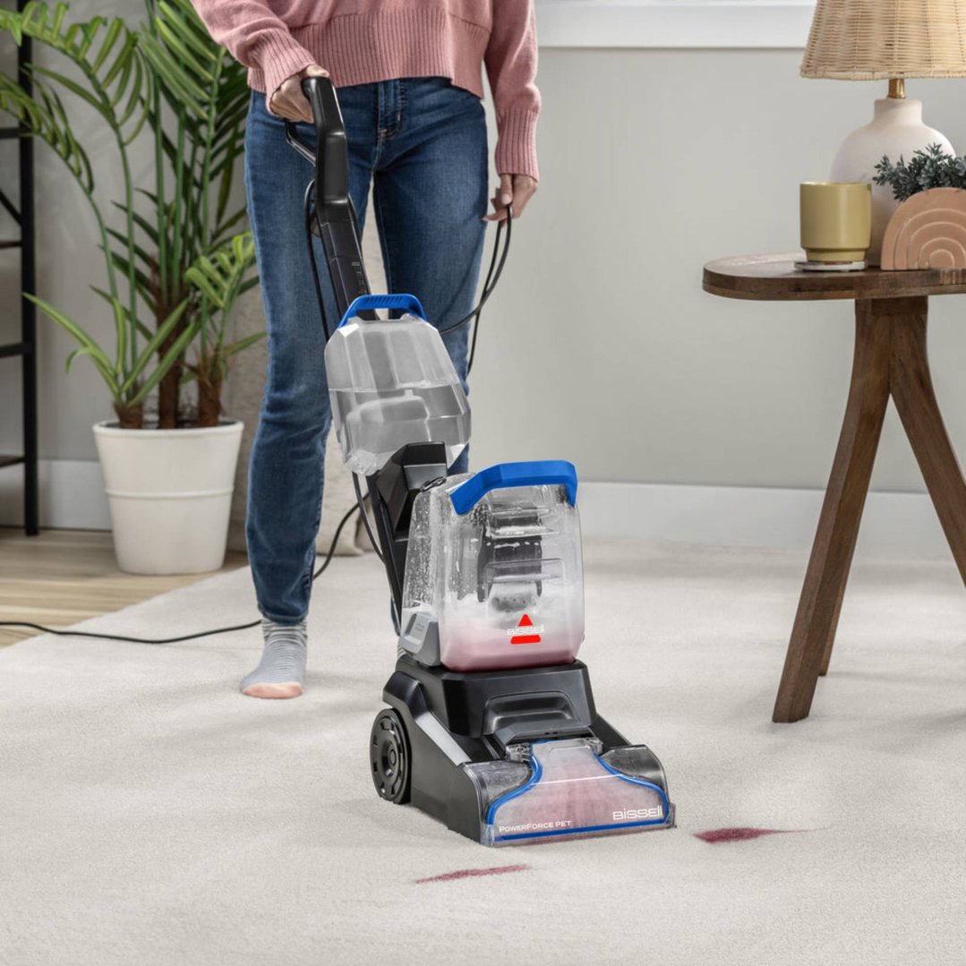 Person using a BISSELL PowerForce Pet upright carpet cleaner on a white carpet