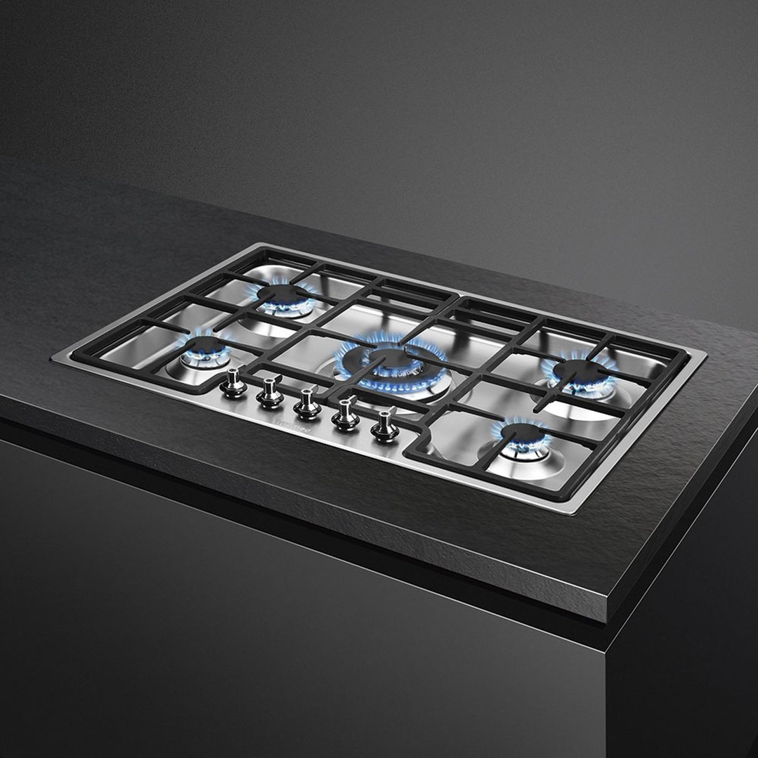 Stainless steel gas cooktop with five burners and controls, built into a dark countertop