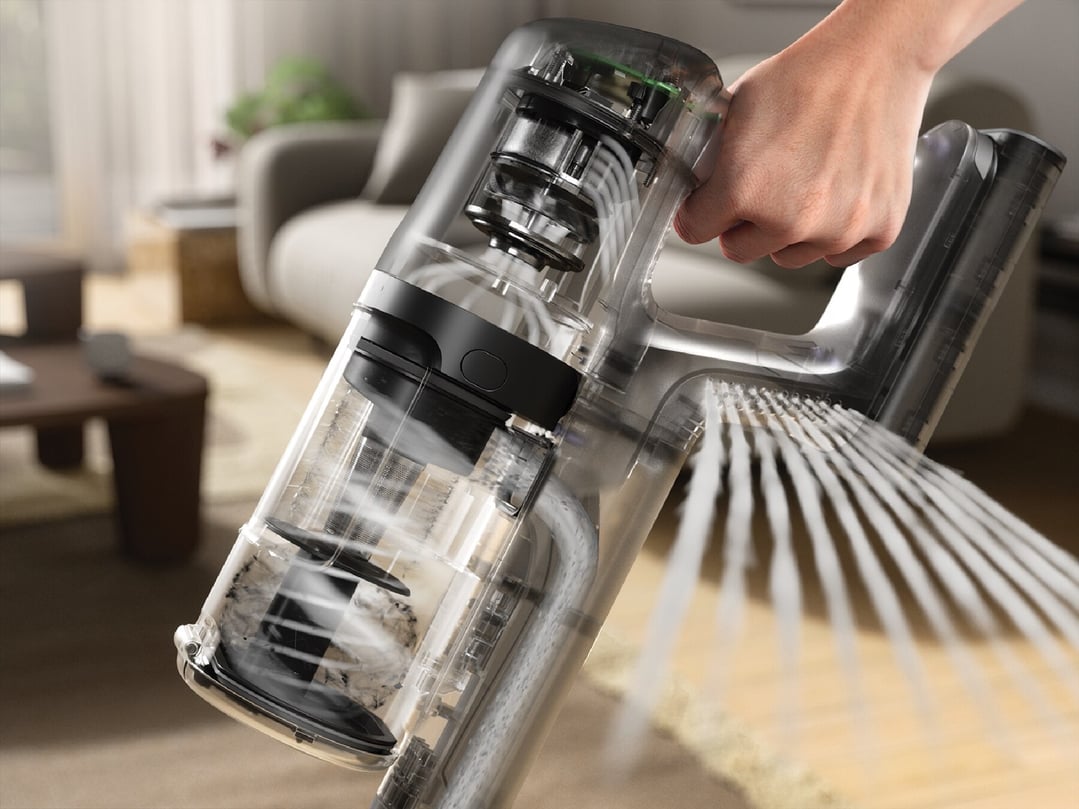Hand holding a transparent cordless vacuum cleaner in a living room setting