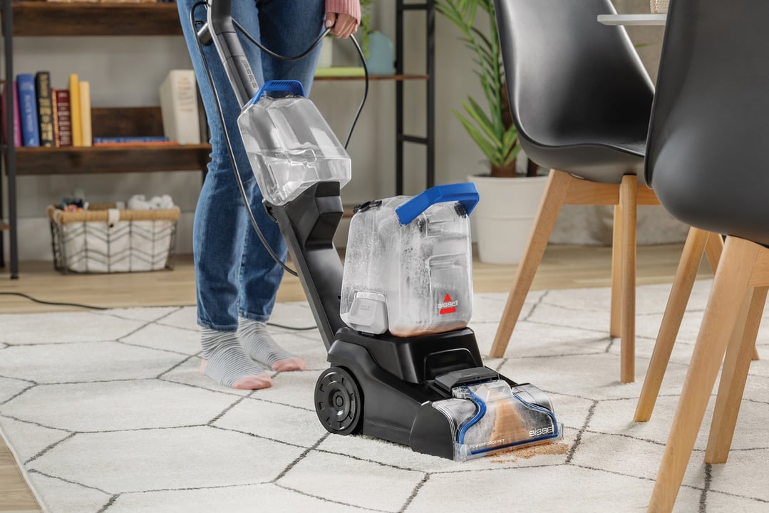 Person cleaning a stain on a white rug with a BISSELL PowerForce Pet upright carpet cleaner