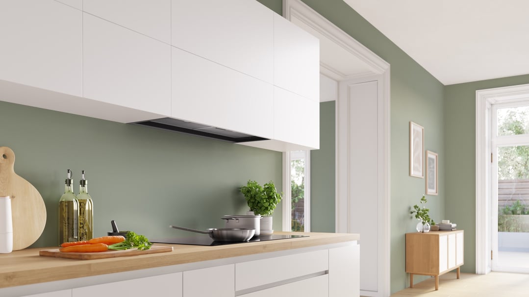 Integrated rangehood above an induction cooktop in a modern kitchen with green walls