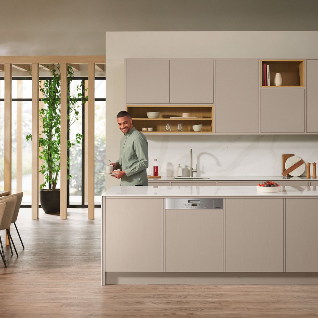 Man holding a mug in a modern kitchen with a built-in dishwasher